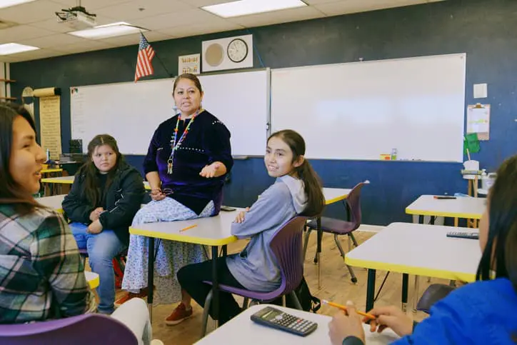 An Indigenous Navajo high school teacher with a group of students in a school classroom.