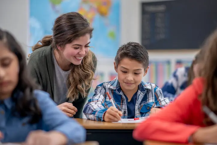 Teacher Helping Student In Elementary Classroom